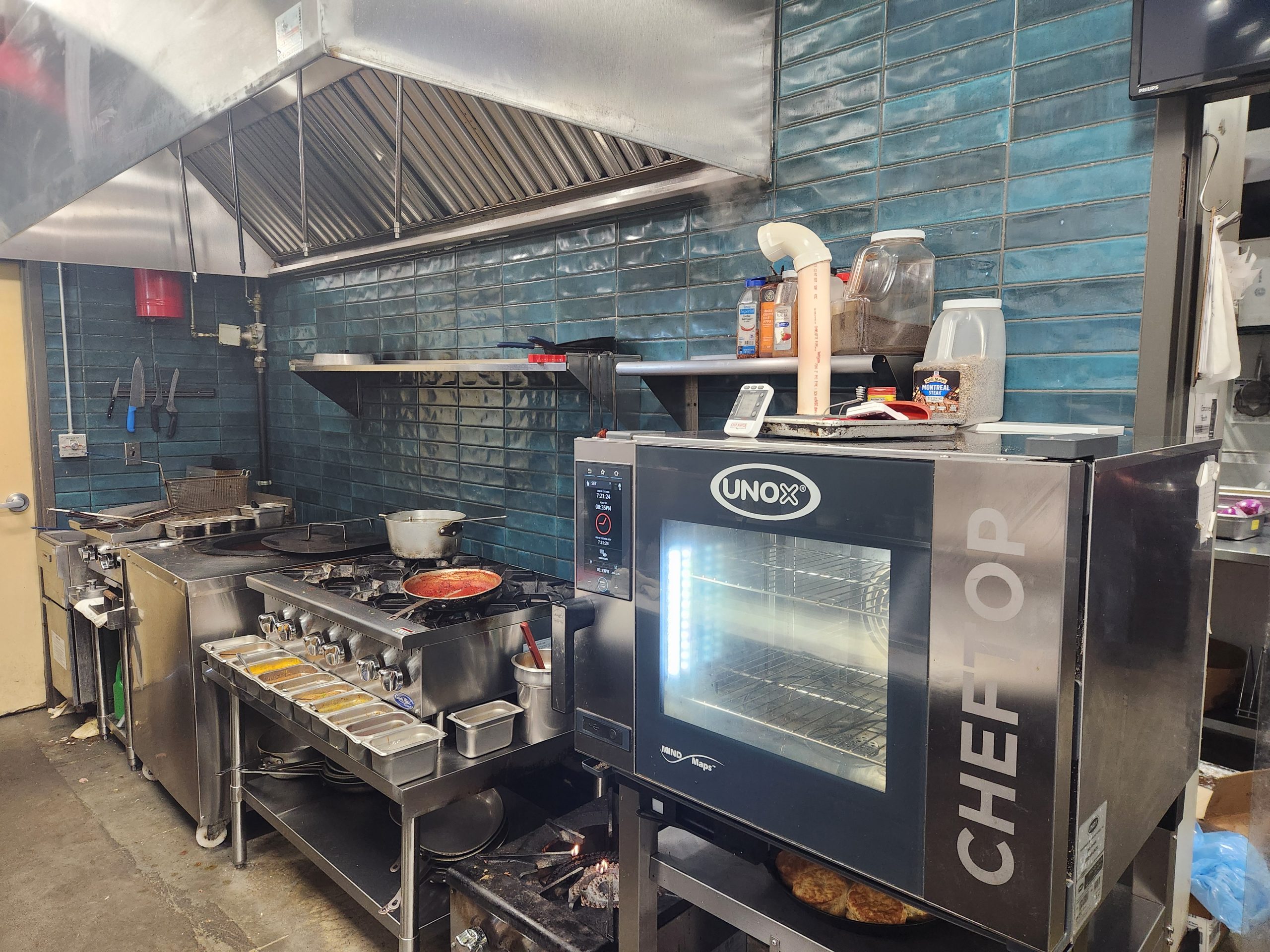 Commercial restaurant kitchen with combi oven, tandoori oven, grill, exhaust hood and fryer sold by the Jimmy Carey Commercial Real Estate Team.