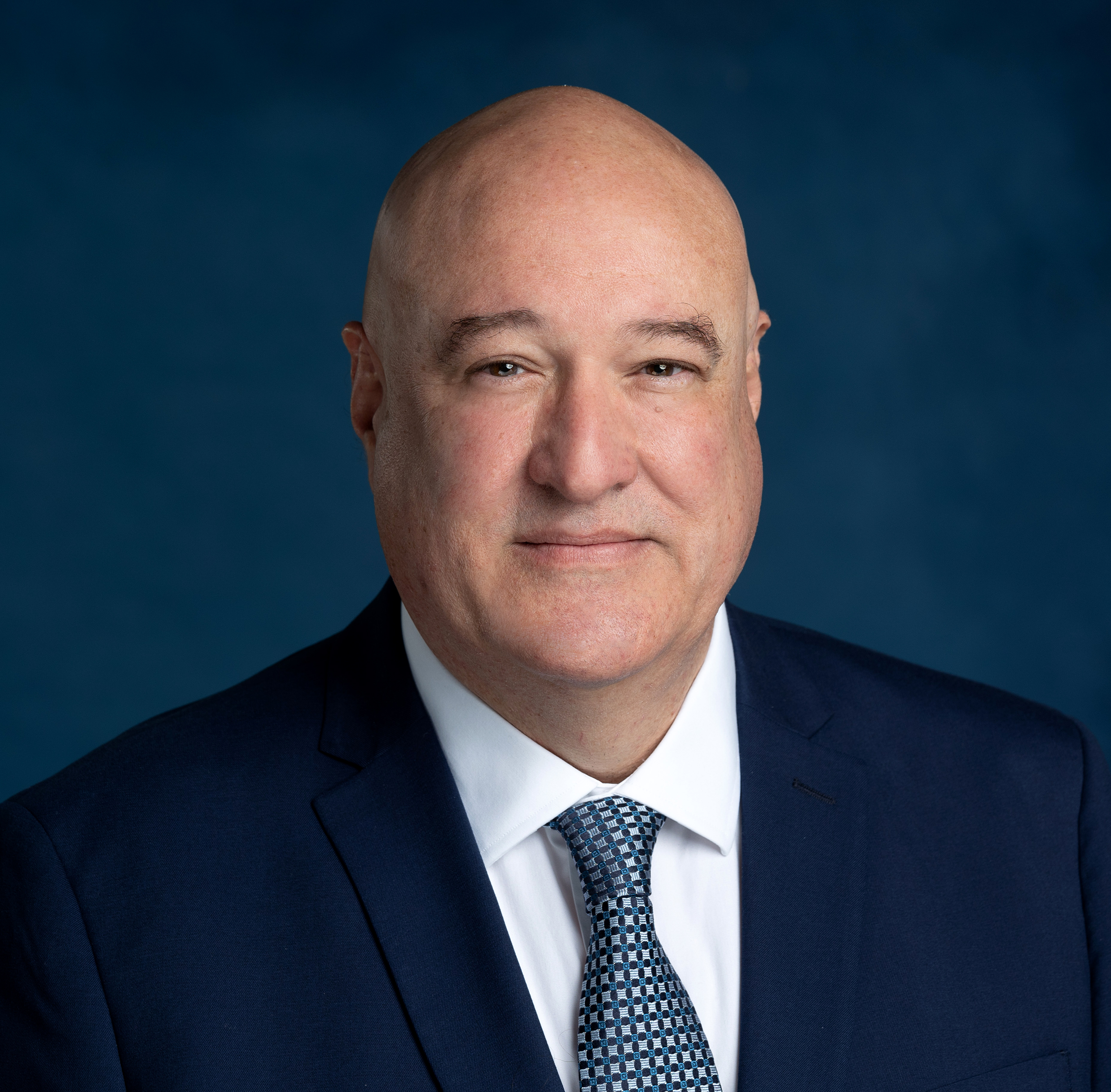Professional headshot of Jimmy Carey, Restaurant Business Broker and Commercial Real Estate Agent, wearing a navy suit, white shirt, and patterned tie against a solid blue background. Representing Jimmy Carey Commercial Real Estate, Atlanta Restaurant Business Broker.